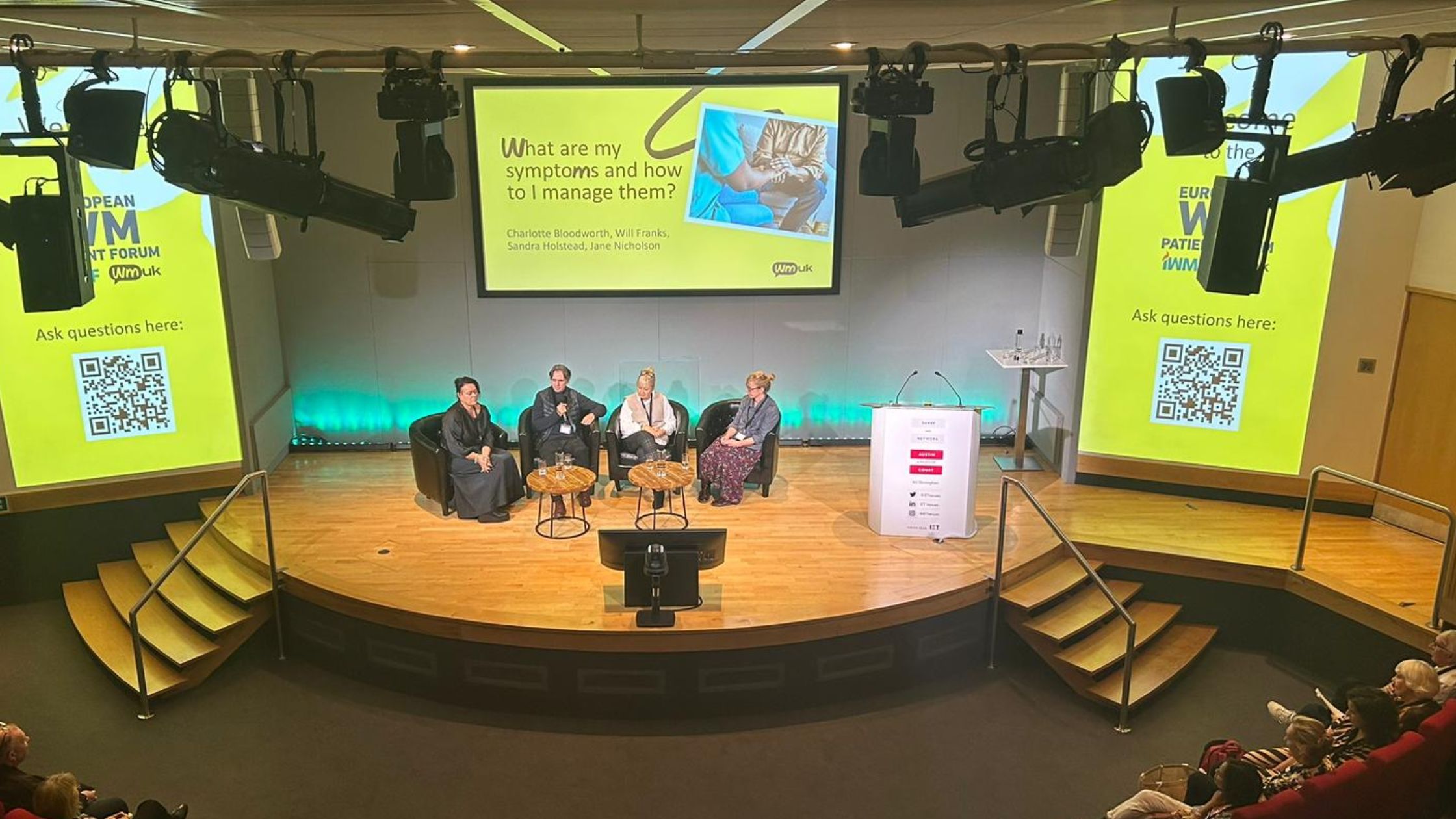 An image of the European WM Patient Forum 2023. A group of people sitting on stage in front of a large screen, engaged in a discussion.